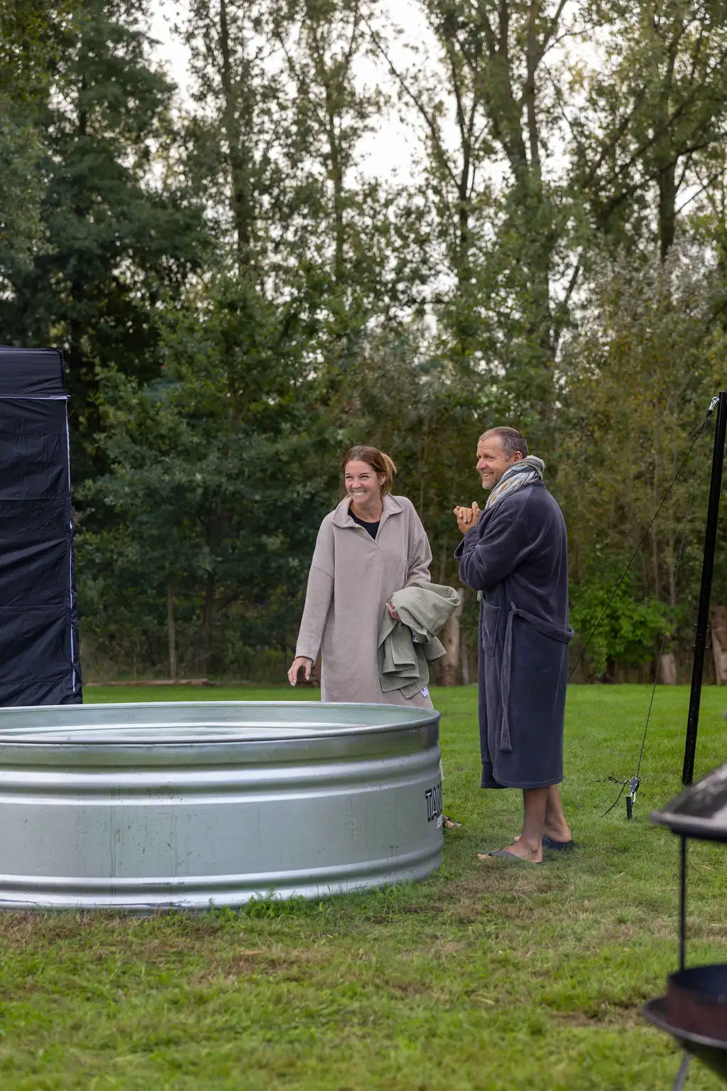 Twee deelnemers in badjas naast het ijsbad, tussen de bomen